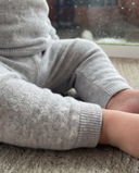 Close up of light grey cashmere pants cuff with small knit heart detail, baby hand resting on carpet