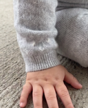 Close up of light grey cashmere pants ribbed cuff with knit heart detail, baby hand resting on carpet