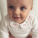 Baby sitting wearing white cotton bodysuit with floral embroidered scalloped collar and white knee socks