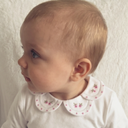 Profile close up of baby wearing white bodysuit with pink floral embroidered scalloped collar