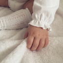 Close up of baby's hand and sleeve cuff, white pointelle knee sock visible in the background