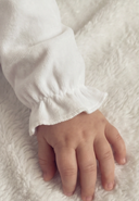 Close up of baby's hand resting on white blanket, ruffled sleeve cuff of sleepsuit
