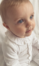 Baby looking up while wearing white pyjama sleepsuit with gold embroidered collar