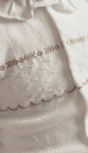 Close up of gold embroidered trim and scalloped hem detail on white sleepsuit fabric