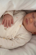 Close up of sleeping baby wearing cream kimono style onesie with tiny toy print, hand resting on chest