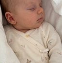 Close up of sleeping baby in cream kimono onesie with wrap front bow tie and tiny toy print