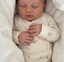Sleeping baby wearing cream kimono onesie with tiny toy print, hands clasped together