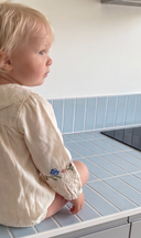 Profile view of toddler wearing ecru bubble romper showing floral embroidered sleeve cuff