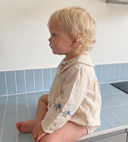 Side profile of toddler sitting on a counter wearing ecru bubble romper with embroidered collar