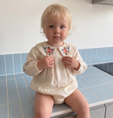 Toddler sitting on a blue tiled counter wearing ecru bubble romper with floral embroidered collar