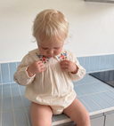 Toddler looking down at floral embroidered Peter Pan collar on ecru bubble romper