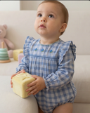 Close up of baby wearing blue plaid romper with embroidered flowers, holding yellow block toy
