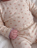 Close up of baby wearing cream floral print top and matching pants, blue trim details