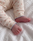Close up of baby feet in cream leggings with soft pink poppy print and blue scalloped cuffs