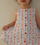 Toddler girl wearing blue and white striped pinafore dress with red rose print, holding out skirt to show heart pockets
