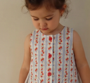 Close up of blue and white striped pinafore dress with red rose print, red buttons and heart shaped pockets, worn by toddler