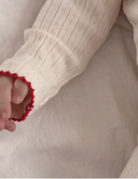 Close up of baby's arm in cream pointelle bodysuit sleeve with red scalloped cuff trim