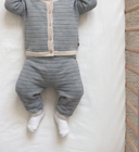 Baby lying down wearing bluey wool knit trousers and matching cardigan with wooden buttons, cream trim, back view