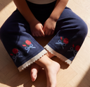 Overhead view of crossed legs in navy knit pants with red rose embroidery and cream ribbed cuffs, on wood floor