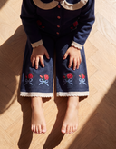 Overhead close up of child sitting wearing navy cardigan and matching pants with red rose embroidery on cuffs and hems