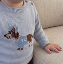 Close up of toddler's shoulder button and dachshund dog intarsia motif on horizon blue wool pullover, hand resting on couch