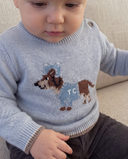 Close up of toddler wearing horizon blue wool pullover with dachshund dog intarsia motif, sitting on a beige couch