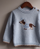 Horizon blue wool pullover with dachshund dog intarsia knit motif, hanging on a wooden hanger against a wall