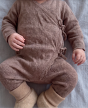 Close up of brown knit wrap romper with tie closure and cream wool booties on baby