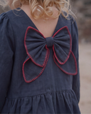 Close up of red stitched bow detail on back of navy dress, cotton gauze fabric