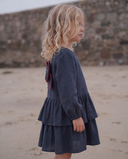 Side profile close up portrait of girl with wavy blonde hair wearing navy dress, beach and stone wall background