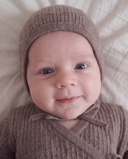 Close up of baby smiling wearing brown knit bonnet and wrap romper with tie closure