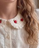 Close up of red rose embroidered collar on cream lace blouse, worn by girl with wavy hair