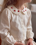 Close up of cream blouse collar with red rose embroidery, worn by child