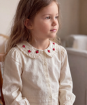 Close up portrait of toddler girl in cream lace blouse with red rose embroidered collar, looking to the side