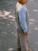 Side profile of child wearing dark brown and white pinstripe pants with blue and gray knit sweater, walking outdoors