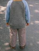 Back view of child wearing dark brown and white pinstripe pants with blue and gray knit sweater, brown boots