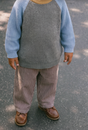 Close up of child wearing dark brown and white pinstripe pants with gray and blue knit sweater, standing outdoors