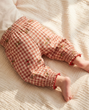 Back of baby wearing red and cream gingham check pants with floral embroidery, lying on quilted blanket