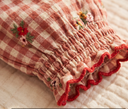 Close up of red and cream gingham check fabric with floral embroidery and red ruffle trim