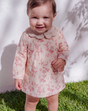 Baby girl wearing pink floral print dress with crochet collar, standing on grass