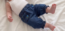 Baby lying down wearing dark wash denim harem pants with floral embroidered pocket and elastic ankle cuffs