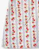 Close-up of a sleeveless top or dress featuring vertical wavy stripes with red and blue floral prints, a heart-shaped chest pocket, and red buttons on a light background.
