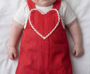 Baby wearing rust red overall with cream heart trim bib over a cream pointelle bodysuit, close up view