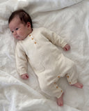 newborn baby in a white cashmere romper laying on a bed