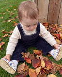 Close up from behind of girl in braided pigtails wearing navy corduroy overalls with embroidered star trim over cream top