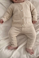 Baby lying down wearing cream merino wool cardigan with button front and matching knit pants, close crop from chin to feet
