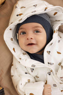 Close up of baby in cream hooded car print jumpsuit and navy knit hat, wrapped in blanket outdoors