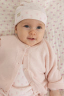 Baby wearing pink knit cardigan and matching hat with small floral print, sitting on floral fabric