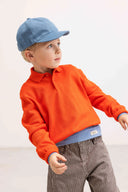 Boy wearing blue baseball cap and orange sweater with dark brown and white pinstripe pants, mid motion