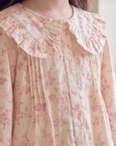 Close-up of a cream-colored long-sleeve blouse with a pink floral print, featuring a large ruffled Peter Pan collar and a button-down front.